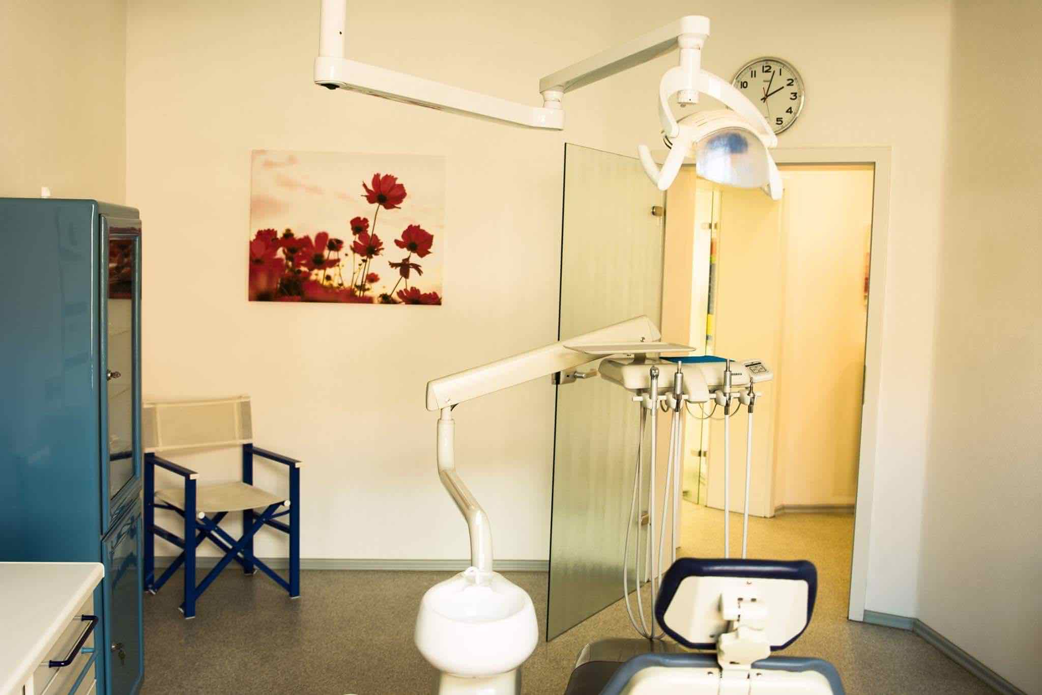 Eines der beiden Behandlungszimmer, mit Behandlungsstuhl im Vordergrund und Eingangstür im Hintergrund.